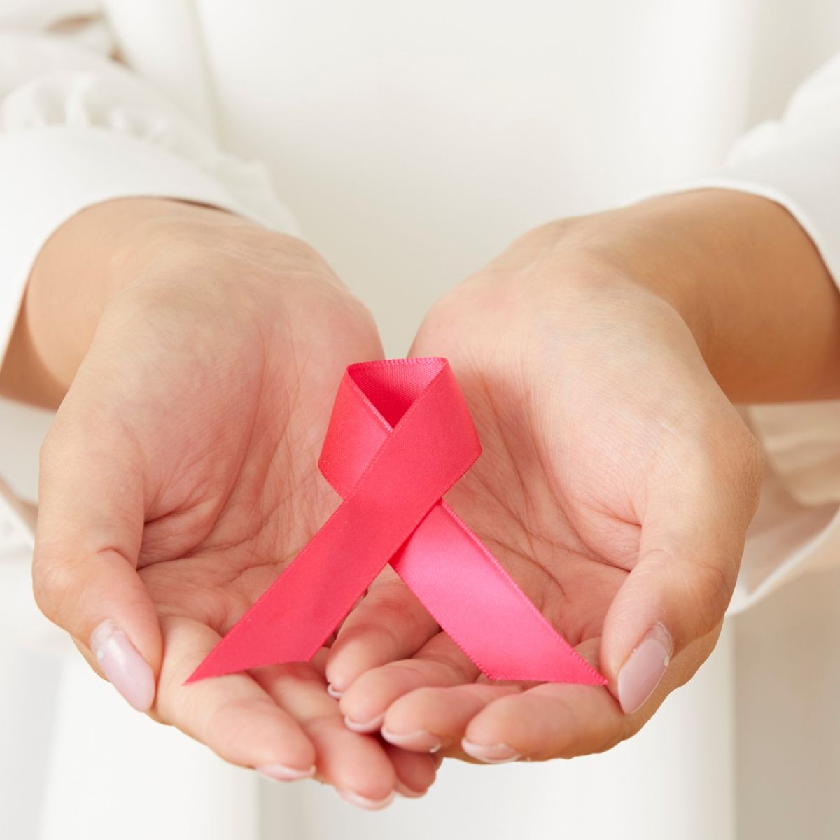 Close-up of a person gently holding a pink breast cancer awareness ribbon in their cupped hands, symbolizing support and awareness.